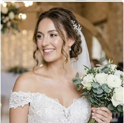 Mariée au chignon bas orné d'un bijou de cheveux, tenant un bouquet blanc